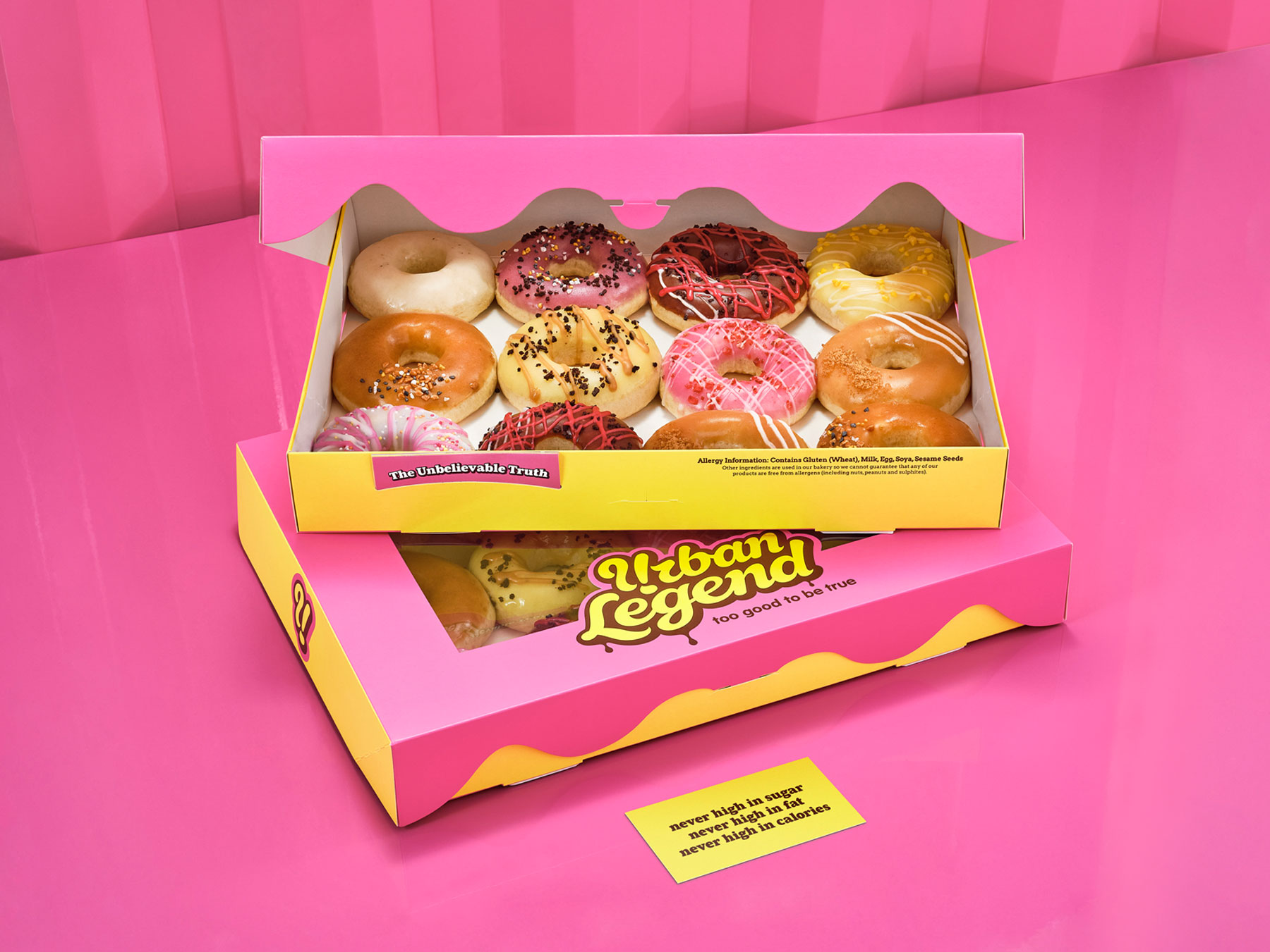 A stack of two Urban Legend donut boxes on a pink background. One box is open showing the donuts design by Biles Hendry